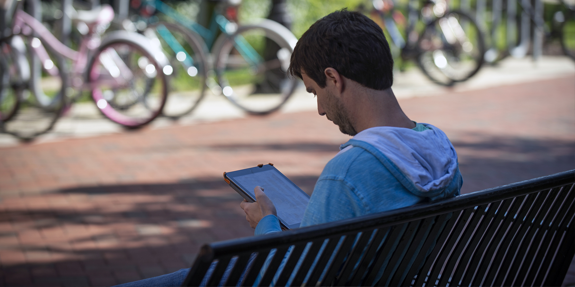 Student sits on bench viewing a tablet outside of University Student Commons, 907 Floyd Avenue.